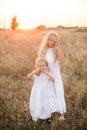 Cute girl with blond long hair with a younger sister in a summer field at sunset