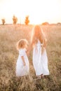 Cute girl with blond long hair with a younger sister in a summer field at sunset