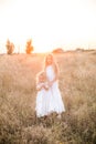 Cute girl with blond long hair with a younger sister in a summer field at sunset