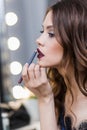 Cute cute girl in a blue dress painted at the mirror, putting on lip pencil professional makeup, makeup, profile, closeup Royalty Free Stock Photo