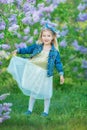 Cute girl in blue jackets with fairy airy skirt standing close to lilac bush Royalty Free Stock Photo