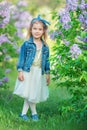 Cute girl in blue jackets with fairy airy skirt standing close to lilac bush Royalty Free Stock Photo