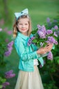 Cute girl in blue jackets with fairy airy skirt standing close to lilac bush Royalty Free Stock Photo