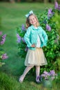 Cute girl in blue jackets with fairy airy skirt standing close to lilac bush Royalty Free Stock Photo