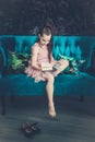 Cute girl with brown hair in a pink dress sitting on a blue sofa and reading a book Royalty Free Stock Photo