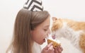 Cute girl celebrates holiday with cake and red cat. Royalty Free Stock Photo