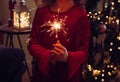 Cute girl child holding sparkler candle in hands in home living room, decorated Christmas tree on background, dark room, lit by sp Royalty Free Stock Photo