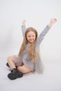 Cute girl child with long blond hair sitting on the floor and yawns sweetly, stretching her hands in different directions on white Royalty Free Stock Photo