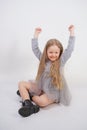 Cute girl child with long blond hair sitting on the floor and yawns sweetly, stretching her hands in different directions on white Royalty Free Stock Photo