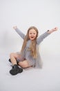 Cute girl child with long blond hair sitting on the floor and yawns sweetly, stretching her hands in different directions on white Royalty Free Stock Photo