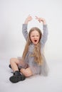 Cute girl child with long blond hair sitting on the floor and yawns sweetly, stretching her hands in different directions on white Royalty Free Stock Photo