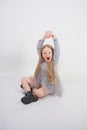 Cute girl child with long blond hair sitting on the floor and yawns sweetly, stretching her hands in different directions on white Royalty Free Stock Photo