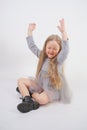 Cute girl child with long blond hair sitting on the floor and yawns sweetly, stretching her hands in different directions on white Royalty Free Stock Photo