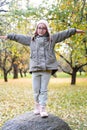 A cute girl climbed a high stone in an autumn apple orchard and depicts an airplane with her hands