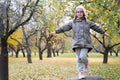 A cute girl climbed a high stone in an autumn apple orchard and depicts an airplane with her hands