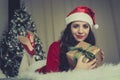 Cute cute girl in clothes santaclaus holding a gift with a green ribbon lying on the bed against the Christmas tree. New year and Royalty Free Stock Photo