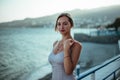 cute girl in cocktail dress stands on a hill overlooking the sea