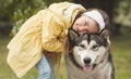 Cute girl sitting on the grass and playing with her funny friend malamute dog