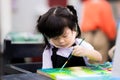 Cute girl is coloring on a canvas. Children work on watercolor art. Child wear black aprons to prevent white school uniforms from