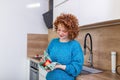 Cute girl with curly red hair whipping her apple with kitchen towel. Young Woman cleaning her fruit in her kitchen. Daily intake