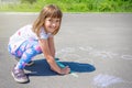 A cute girl draws colored chalk on asphalt. Children`s drawing