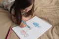 Cute girl draws a pencil drawing. A child learns to draw people. The child lies on the bed and draws with a blue pencil Royalty Free Stock Photo