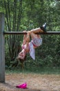 Cute girl in dress and shorts hanging up side down at a climbing frame outdoors.