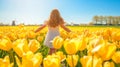 Cute girl in dress walking in the field of yellow tulips windmill in the background. Blue sky sunlight summer day Royalty Free Stock Photo