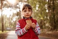 Cute girl eating ice cream walking in forest, wearing red casual outfit, looks in distance with serious facial expression, posing Royalty Free Stock Photo