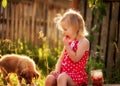 A cute girl eats raspberries and a little puppy next to her.