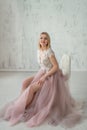 Cute girl in an evening dress with lace and pink fartine on the background of a white textural wall. Girl in a evening