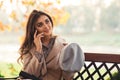 Cute girl flirts while talking on the phone with her boyfriend. Pretty woman sitting on the bench in autumn park Royalty Free Stock Photo