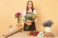 Cute girl florist collecting bouquet in flower shop, beautiful florist creating composition of flowers wearing brown apron Royalty Free Stock Photo