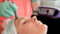 Cute girl gets facial treatments against. The procedure in the beauty salon. Beautician uses a microcurrent therapy hydrating gel