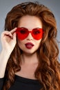 Cute girl with glasses in the shape of a heart. Funny, positive, funny model in red sunglasses. Royalty Free Stock Photo