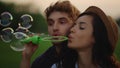 Cute girl and guy throwing bubbles on field. Couple blowing soap bubbles