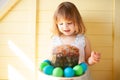 Cute girl with Easter eggs and Easter cake with yellow wooden background