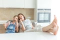 Cute girl and her mother are smiling while eating ice cream in the kitchen with legs on a table