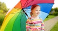 Cute girl holding colorful rainbow umbrella on rainy summer day. Child walking under warm rain outdoors. Outdoor summer activities Royalty Free Stock Photo