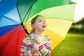 Cute girl holding colorful rainbow umbrella on rainy summer day. Child walking under warm rain outdoors. Outdoor summer activities Royalty Free Stock Photo