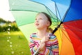 Cute girl holding colorful rainbow umbrella on rainy summer day. Child walking under warm rain outdoors. Outdoor summer activities Royalty Free Stock Photo