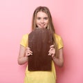 Cute girl holding and eating giant cocoa chocolate bar near pink wall.