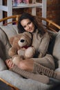 Cute girl in knee socks and sweater with Teddy bear in her hands sitting in armchair in fancy room Royalty Free Stock Photo