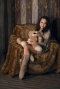 Cute girl in knee socks and sweater with Teddy bear in her hands sitting in armchair in wooden room Royalty Free Stock Photo