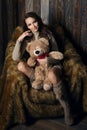 Cute girl in knee socks and sweater with Teddy bear in her hands sitting in armchair in wooden room Royalty Free Stock Photo