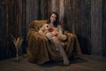 Cute girl in knee socks and sweater with Teddy bear in her hands sitting in armchair in wooden room Royalty Free Stock Photo