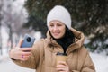 Cute girl laughing and making a video call outside in winter. Hold a disposable cup of coffee