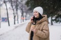 A cute girl is laughing and talking on the phone outside in winter . Hold a disposable cup of coffee