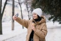 A cute girl laughs and takes a selfie outside in winter. Hold a disposable cup of coffee