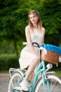 Cute girl posing while sitting on a vintage blue bicycle with basket in the city park Royalty Free Stock Photo